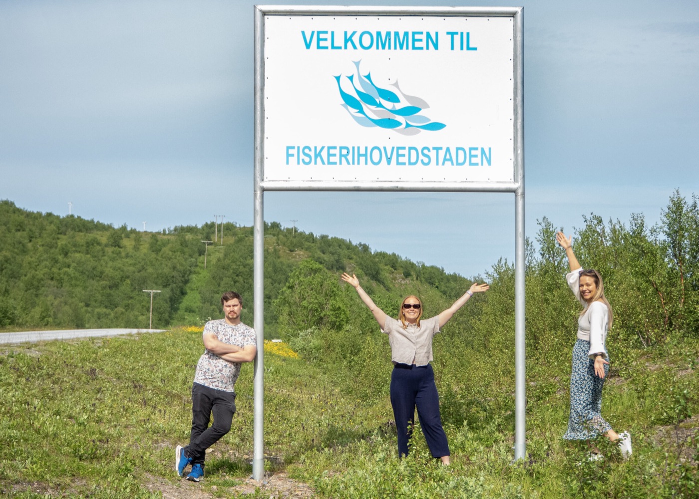Tre personer jubler foran skiltet «Velkommen til Fiskerihovedstaden»